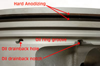 Here's a 'bare' LS3 piston. The hard-anodizing adjacent to the top ring groove is a durability feature. While the oil drainback notches have been in Gen 3/4 pistons for along time, new are the oil drainback holes, two each on above the major and minor thrust faces, drilled into the piston interior.<br />Image:  Author.