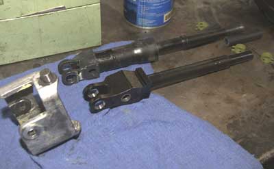Top is the O.E. shifter. It's a two-piece unit with the upper and lower sections joined with a rubber coupling inside the area near the top of the larger-diameter, lower section. The Hurst ditches the rubber coupling, has a shorter lever but a longer distance between the lever pivot point and the shift rod connection. Those different dimensions is what shortens the throw. The silver part at left is the stock cardian joint or pivot. The Hurst retains that part. Image: Author.